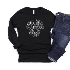 May include: Black long-sleeve shirt with a white sunflower graphic. The graphic features three sunflowers in a sketched style. The shirt is paired with dark wash blue jeans. The shirt is made of a soft, comfortable material.