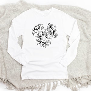 May include: White long-sleeve shirt featuring a black and white floral design of three sunflowers. The shirt is made of a soft material and is suitable for casual wear. The design is centered on the front of the shirt.
