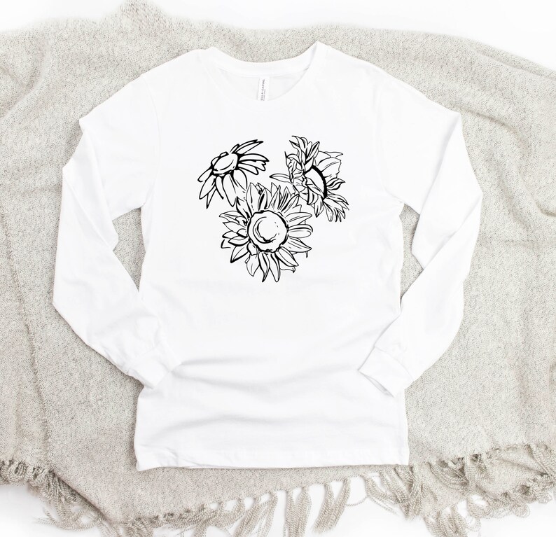May include: White long-sleeve shirt featuring a black and white floral design of three sunflowers. The shirt is made of a soft material and is suitable for casual wear. The design is centered on the front of the shirt.