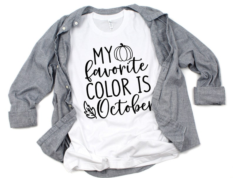 May include: White t-shirt with the text "MY favorite COLOR IS October" in black script, featuring a pumpkin and leaf graphic. A gray button-down shirt is draped over the t-shirt.