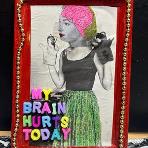 May include: A framed collage featuring a black and white image of a person with a pink brain illustration on their head, wearing a black top and green skirt. The text MY BRAIN HURTS TODAY is in colorful plastic letters. Gold beads line the red frame.