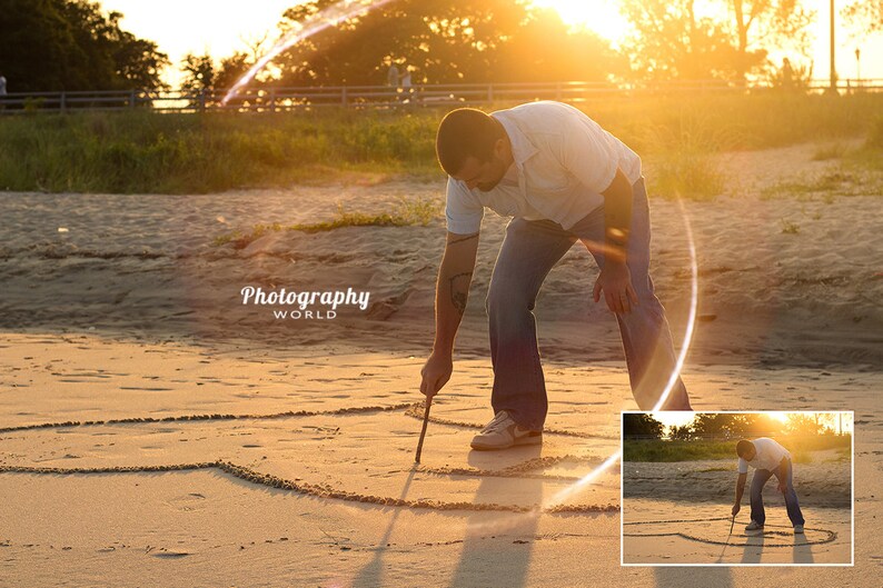 May include: A person draws a heart shape in the sand on a beach at sunset. The sun is shining brightly and creating a lens flare effect. The person is wearing a white shirt and blue jeans.