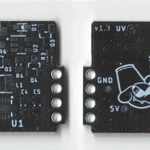 May include: A black circuit board with white text and components. The board has a small cartoon character with a hat and a mustache. The text on the board includes "V1.3 UV", "EN", "GND", "SW", "VCC", and "SV".