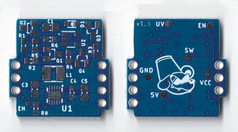 May include: A blue circuit board with various components, including resistors, capacitors, and an integrated circuit labeled "U1". The board has a white outline and a white text label "v1.3" in the upper right corner. The board also features a white cartoon illustration of a creature with a hat.