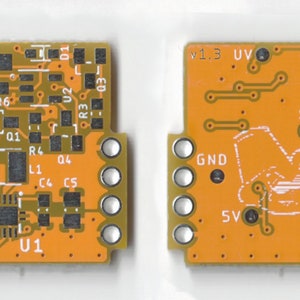 May include: Close-up of an orange printed circuit board with electronic components, including a chip labeled "U1", resistors, capacitors, and a switch labeled "EN". The board has a version number "v1.3" and a label "UV".
