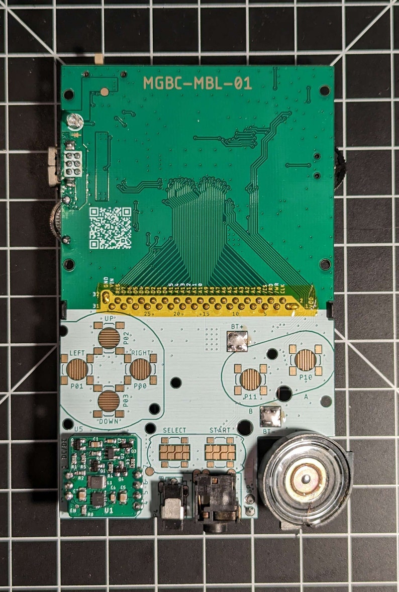 May include: A green circuit board with the text "MGBC-MBL-01" printed on it. The board has a variety of components, including buttons, a speaker, and a chip labeled "U1".