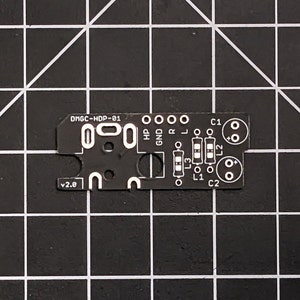 以下が含まれることがあります： 白い文字とマークがついた黒い回路基板。テキストには「DMGC-HDP-01」と「v2.0」と記載されています。いくつかの丸い穴と長方形の部品スペースがあります。