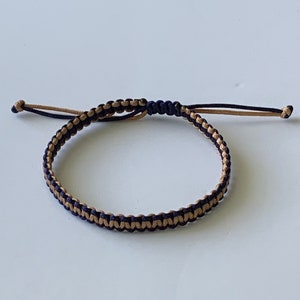 May include: A black and gold braided friendship bracelet with a knot closure.