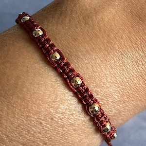 May include: A red cord bracelet with gold beads. The bracelet is adjustable with a sliding knot.