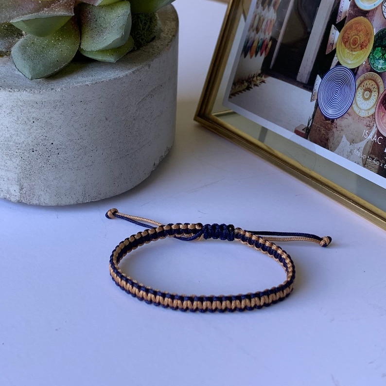 May include: A navy blue and gold braided friendship bracelet. The bracelet is made with two strands of cord, one navy blue and one gold.