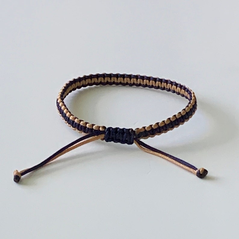 May include: A black and brown braided bracelet with adjustable ties.