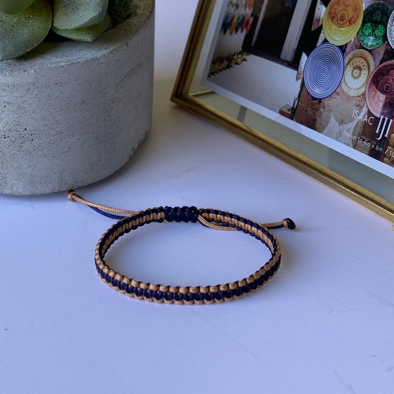 May include: A navy blue and gold braided friendship bracelet with a knot at the end.