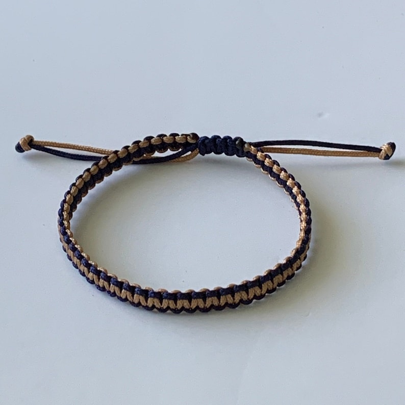 May include: A black and gold braided friendship bracelet with a knot closure.