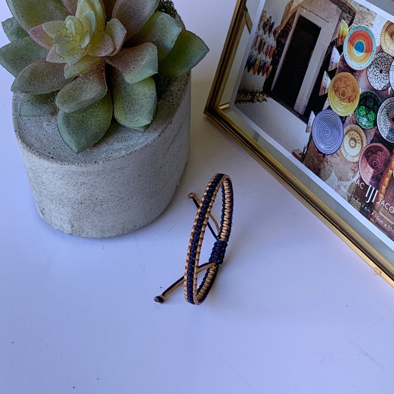 May include: A blue and gold braided friendship bracelet. The bracelet is made of two strands of cord, one blue and one gold, that are woven together.