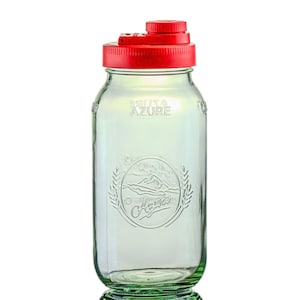 May include: A clear glass jar with a red lid. The jar has a wide mouth and a cylindrical shape. The jar has the word "Azure" printed on it. The jar has a decorative emblem with the word "Agave" on it.