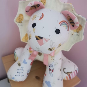 May include: A handmade stuffed lion toy with a white body and a patterned mane and ears. The lion's body is decorated with bees, rainbows, and the text "my smiles begin with you". It has a pink bow and button details.