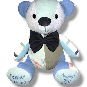 May include: A patchwork teddy bear with a black bow tie. The bear is made from blue, green, and grey fabrics. The left foot reads "Jasper Monroe" and the right foot reads "August 2nd 2022". A dinosaur print is visible.