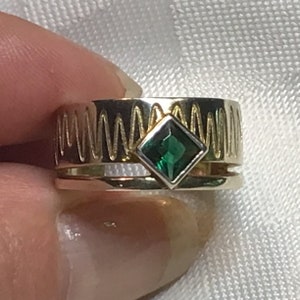 May include: A gold and silver ring with a green gemstone set in the centre. The ring has a textured band with a wavy design.