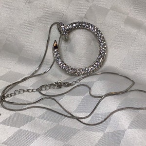 Chic long chain necklace with pendant representing a nail in a circle decorated with small colorless rhinestones.