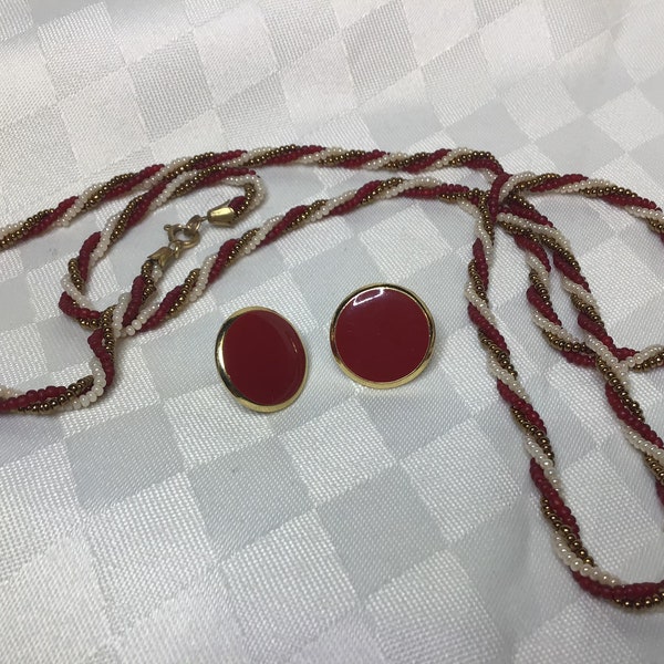 Ensemble collier de petites billes de verre, trois rangs avec attache de métal dorée. Boucles d’oreilles clips métal dorés émaillés rouge.