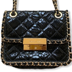 May include: Black quilted handbag with a snakeskin pattern. The bag features gold-tone chain straps and hardware, including a rectangular clasp with the "MICHAEL KORS" logo.