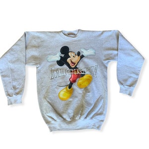 May include: A gray sweatshirt with a graphic print of Mickey Mouse in a red and yellow outfit. The text "MICKEY" is printed in silver below the image.