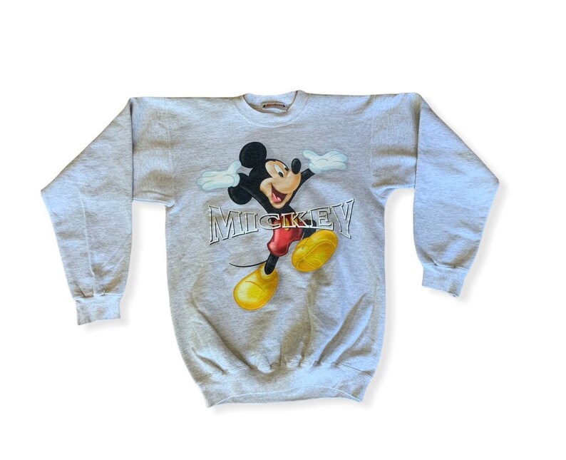 May include: A gray sweatshirt with a graphic print of Mickey Mouse in a red and yellow outfit. The text "MICKEY" is printed in silver below the image.