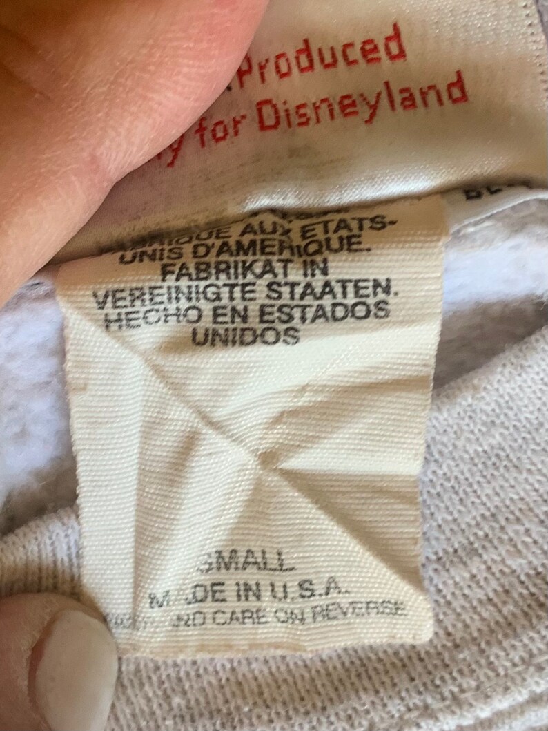 May include: White tag with black text that reads "Produced for Disneyland" and "Small Made in U.S.A. and care on reverse". The tag also has text in French, German, and Spanish.