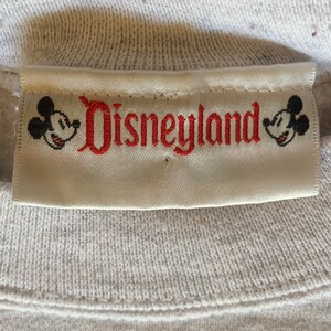 May include: White label with red embroidered text "Disneyland" and Mickey Mouse heads on either side.