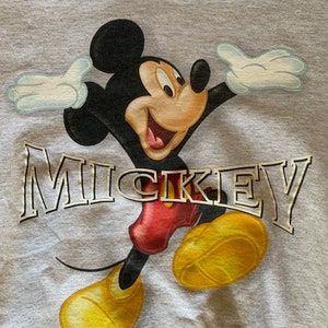 May include: A gray sweatshirt with a cartoon image of Mickey Mouse in a red and yellow outfit. The word "MICKEY" is printed in gold letters on the front of the sweatshirt.