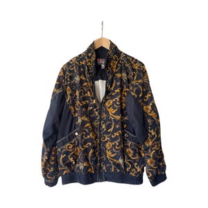 May include: A black and gold patterned jacket with a zipper closure. The jacket has a stand-up collar and a ribbed hem.
