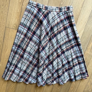 May include: A knee-length plaid skirt in a classic style. The skirt features a pleated design and a pattern of intersecting lines in shades of gray, red, blue, and white. The skirt is made of a soft, woven fabric.