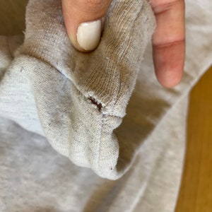 May include: Close-up of a light gray sweatshirt with a small hole in the fabric.