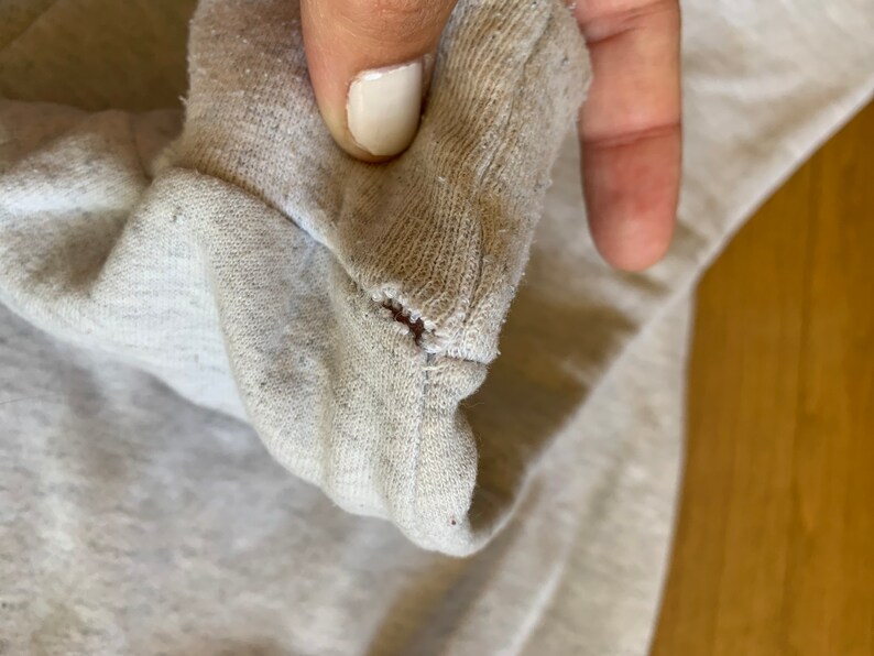May include: Close-up of a light gray sweatshirt with a small hole in the fabric.