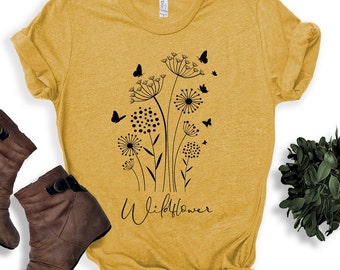 May include: A mustard yellow t-shirt with a black graphic of dandelions and butterflies. The text "Wildflower" is printed below the graphic.