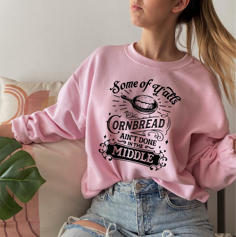 May include: Pink sweatshirt with a black graphic that says "Some of Y'all's Cornbread Ain't Done in the Middle".