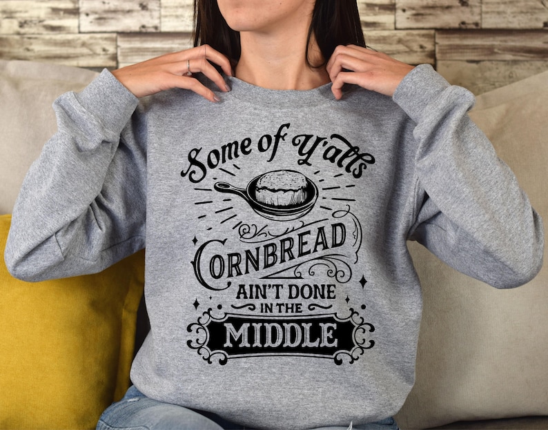 May include: Gray sweatshirt with a black graphic design that says "Some of y'all's cornbread ain't done in the middle". The graphic also includes a drawing of a pan of cornbread.