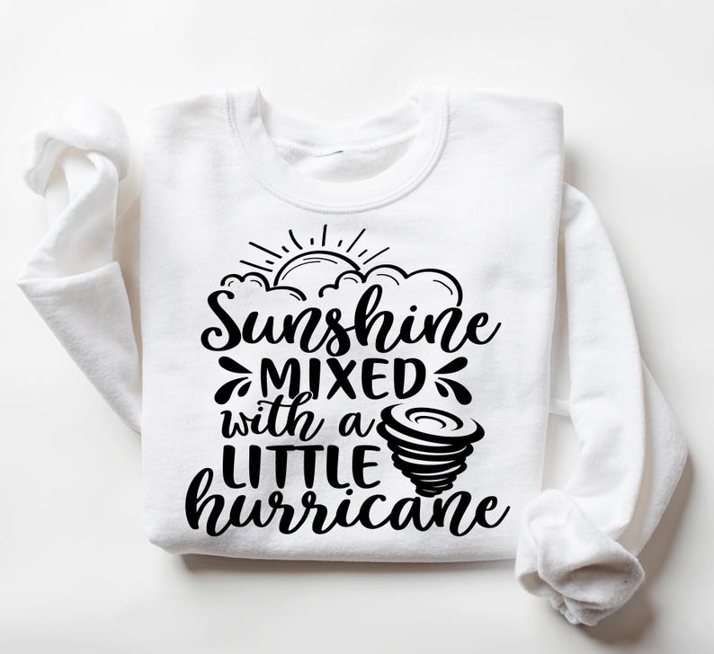 May include: White sweatshirt with the phrase "Sunshine mixed with a LITTLE hurricane" in black script. The design includes a sun, clouds, and a tornado graphic. The sweatshirt has long sleeves and a crew neck.