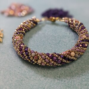 May include: A purple, pink and gold beaded bracelet with a twisted design.
