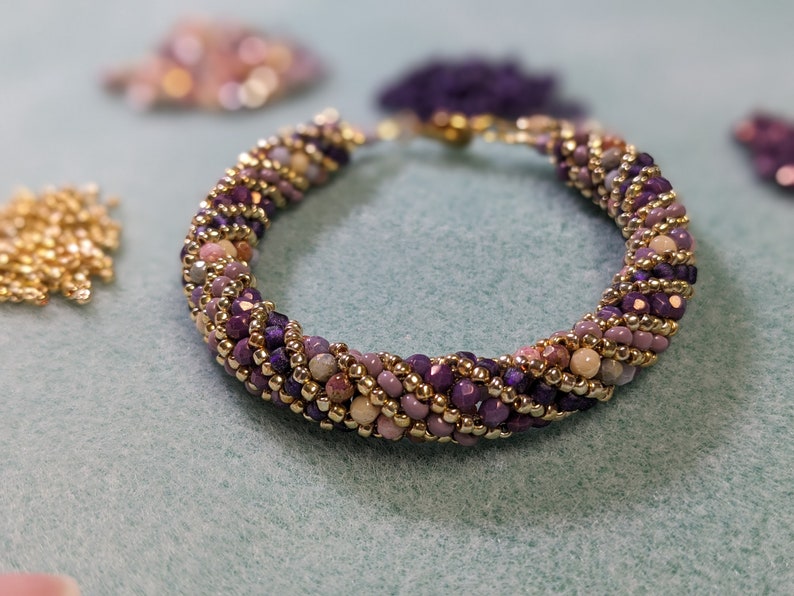 May include: A purple, pink and gold beaded bracelet with a twisted design.
