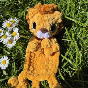 Peut inclure: Une peluche lion faite à la main, de couleur orange et marron, posée dans l'herbe verte avec des marguerites blanches. Le lion a de grands yeux noirs, un museau blanc et une crinière touffue. Le jouet est doux et câlin.