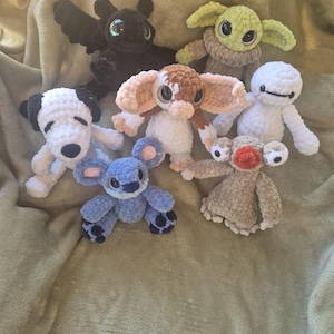 May include: A collection of six crocheted plush toys featuring a black dragon, a green alien, a white and black dog, a brown and white creature with large ears, a blue koala-like character, and a white robot with a round head and black eyes.