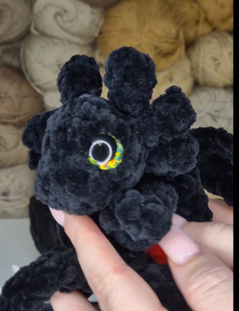 May include: Black crocheted plush toy with a large, colorful eye. The toy is made of soft, fuzzy yarn and has a textured surface.