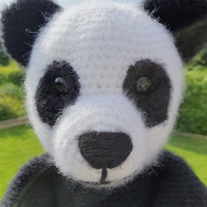 Op de afbeelding: Een gehaakt pandabeer speelgoed met zwart en wit bont. De panda heeft zwarte ogen en een zwarte neus.