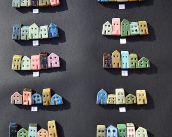 Puede incluir: Diez conjuntos de figuras de casas de cerámica en miniatura dispuestas en filas, cada conjunto contiene cinco casas pequeñas en varios colores, incluyendo azul, verde, rosa, amarillo y blanco. Cada conjunto tiene una etiqueta blanca numerada del uno al diez.