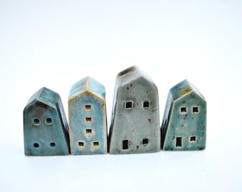 Puede incluir: Cuatro pequeñas figuras de casas de cerámica dispuestas en fila. Las casas presentan un esmalte azul verdoso brillante con patrones de grietas visibles y motas oscuras. Cada casa tiene pequeños recortes cuadrados que representan ventanas.