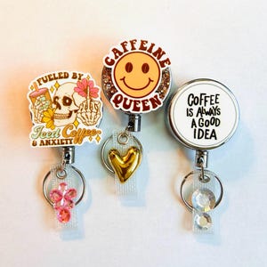 May include: Three retractable badge holders with different designs. One says "Fueled by Iced Coffee & Anxiety" with a skull graphic. Another says "Caffeine Queen" with a smiley face. The third says "Coffee is Always a Good Idea".