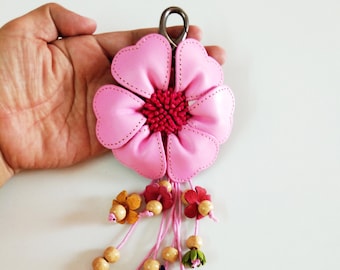 May include: Pink leather flower keychain with a pink string and wooden beads. The flower has a pink center with a red and white design. The keychain has a silver metal ring.