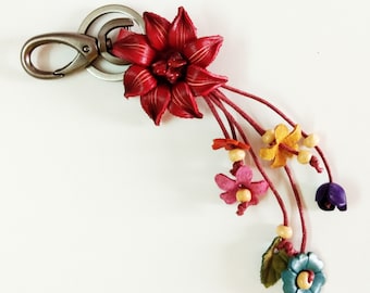 Könnte beinhalten: Ein schlüsselanhänger mit floralem Thema und einem silbernen Verschluss. Der Schlüsselanhänger zeigt eine große, tiefrote Blume und mehrere kleinere, bunte Blumen in Rosa, Gelb, Blau und Lila. Holzperlen akzentuieren das Design.