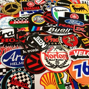 May include: A collection of colorful embroidered patches featuring various logos and designs, including motorcycle brands, racing teams, and vehicle manufacturers. The patches are made of fabric and have a variety of shapes and sizes.